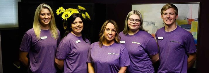 Chiropractor Bloomington IL Jess Bruin With Team In Front Of Dark Wall Chiropractor Bloomington IL Jess Bruin With Team In Front Of Dark Wall